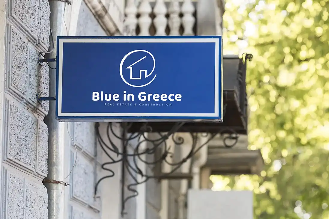 A blue Blue in Greece sign mounted on a stone wall among green foliage