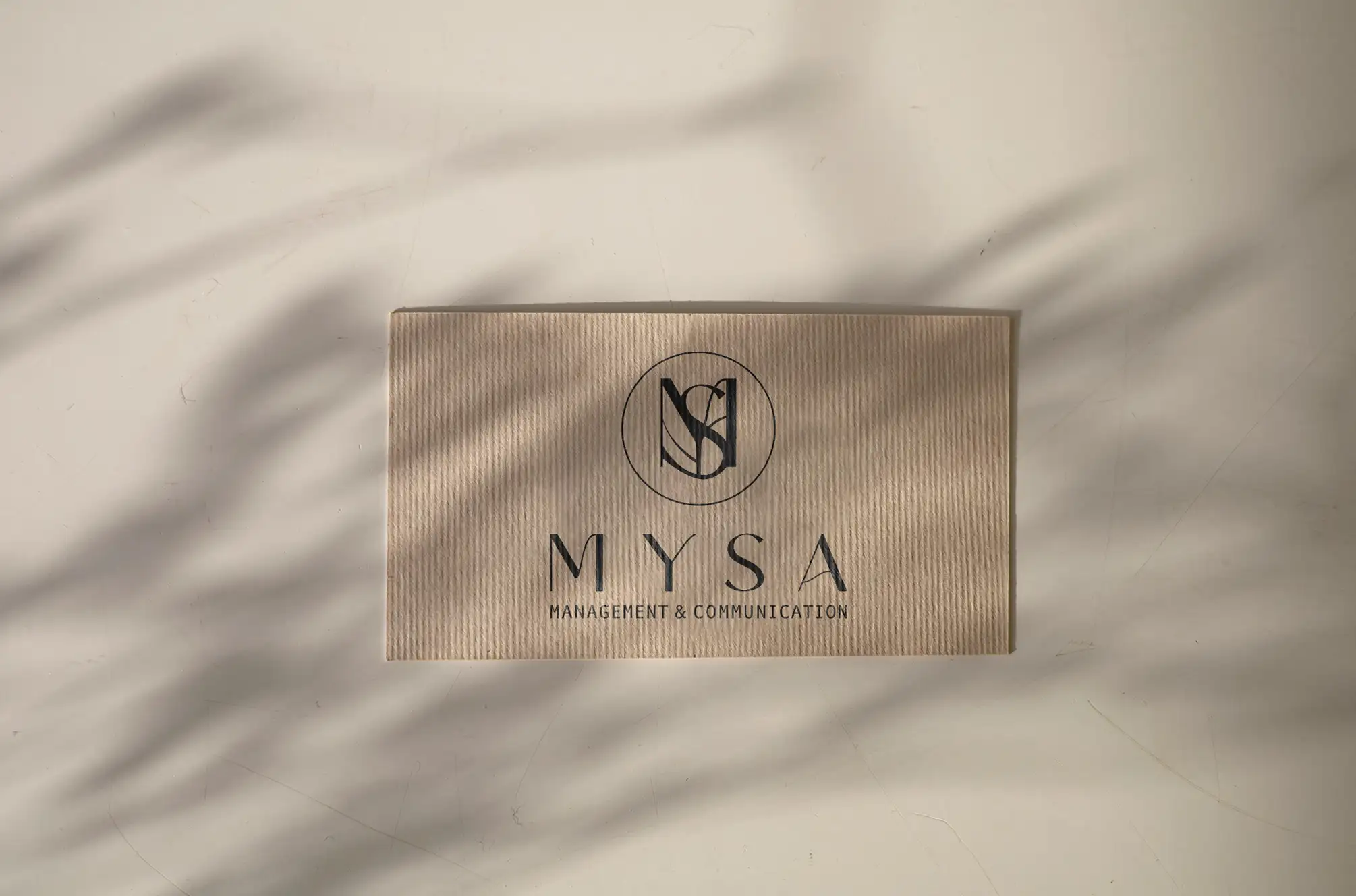 The MYSA monogram and wordmark debossed on a ribbed kraft box under soft palm-leaf shadows
